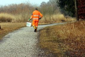 man in orange uniform walking in forest with big bucket