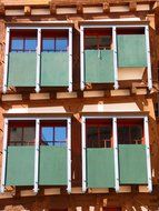 windows with green mechanical shutters on wooden facade
