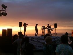 musicians on stage at the beach at sunset