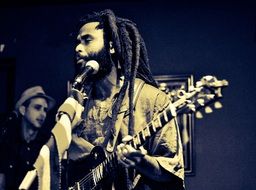 singer with dreadlocks playing guitar