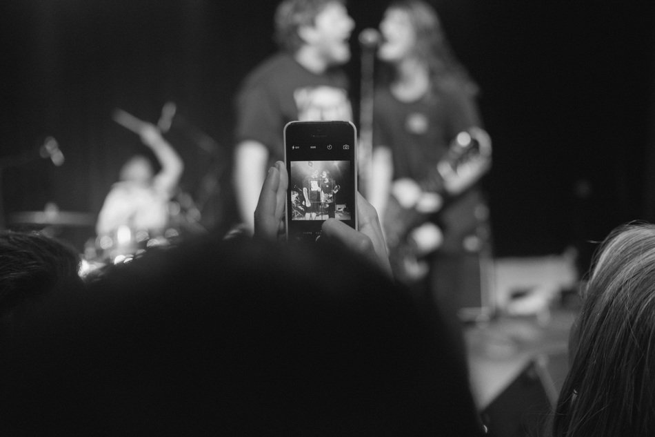 person taking photo of musicians on concert with smartphone