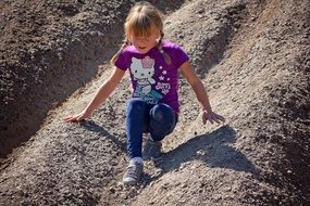 Blonde child girl slipping on the sand hill