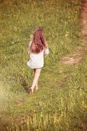 girl goes away by path in grass