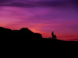 two persons with bikes silhouettes at purple sky