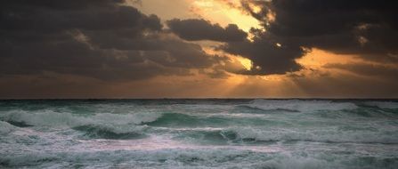 ocean waves and sun in clouds into the storm