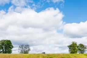 cloudscape two persons sitting on bench in yellow field