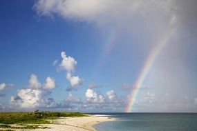 Beautiful and colorful rainbow on a beach under blue sky with white clouds