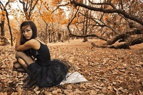 girl in a black dress and torn tights in the autumn park