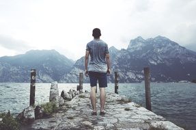 Young man by lake near the beautiful mountains under cloudy sky