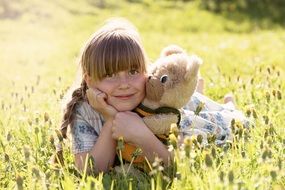 girl is hugging a teddy bear in a meadow
