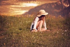 Little girl in a broad-brimmed hat with long hair on meadow