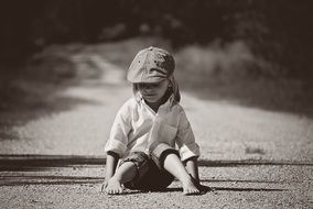 Black and white photo of a child sitting on the road