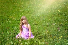 Little girl in a beautiful dress with long hair amid the meadow in the sun