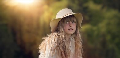 little blonde in a hat on nature on a blurred background