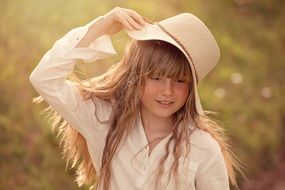 Little girl with long hair in a hat in the rays of the evening sun