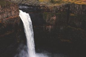 foaming waterfall streaming from dark cliff