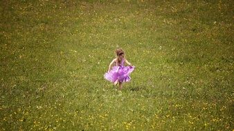 Little girl in a beautiful dress runs through a meadow