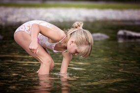 Little girl in a swimsuit plays in the water of a lake