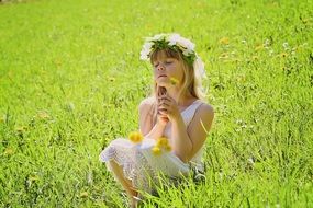 Little girl in a wreath amongst a green meadow on a sunny day