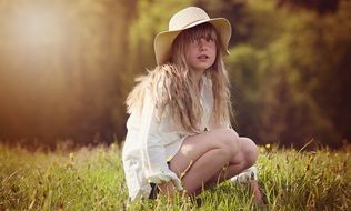 Little girl with long curly hair and a hat in the meadow