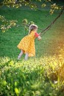 Little girl in a yellow dress is playing on a tree branch