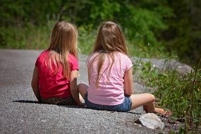 two cute girls sitting on road back view