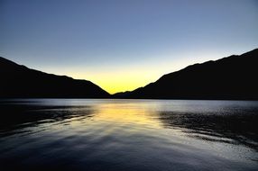 evening mountain lake against the yellow sun on the horizon