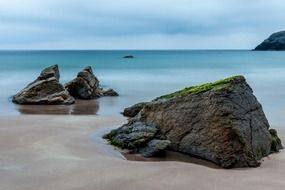 black rocks on beach at calm sea, uk, scotland