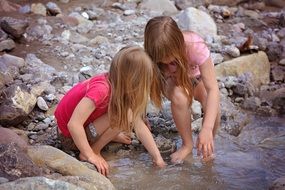 Blonde two girls on the shore of a mountain stream