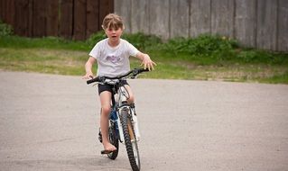 Little girl is riding a bike on the path near the fence