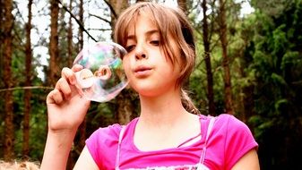 young girl in pink blowing bubbles