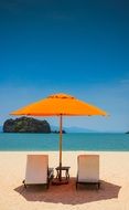 two loungers and an orange beach umbrella on the ocean