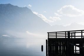 Beautiful pier in fog above the lake with the mountains on background