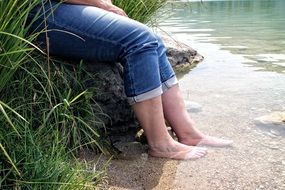 Feet of a man in the water on the lake shore with plants