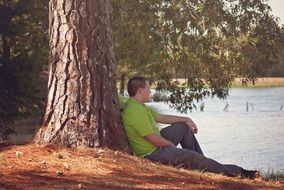 photo of A man sits under a tree near the lake