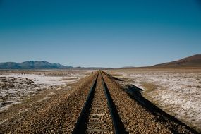 Beautiful railway tracks in sunny desert under blue and white sky background