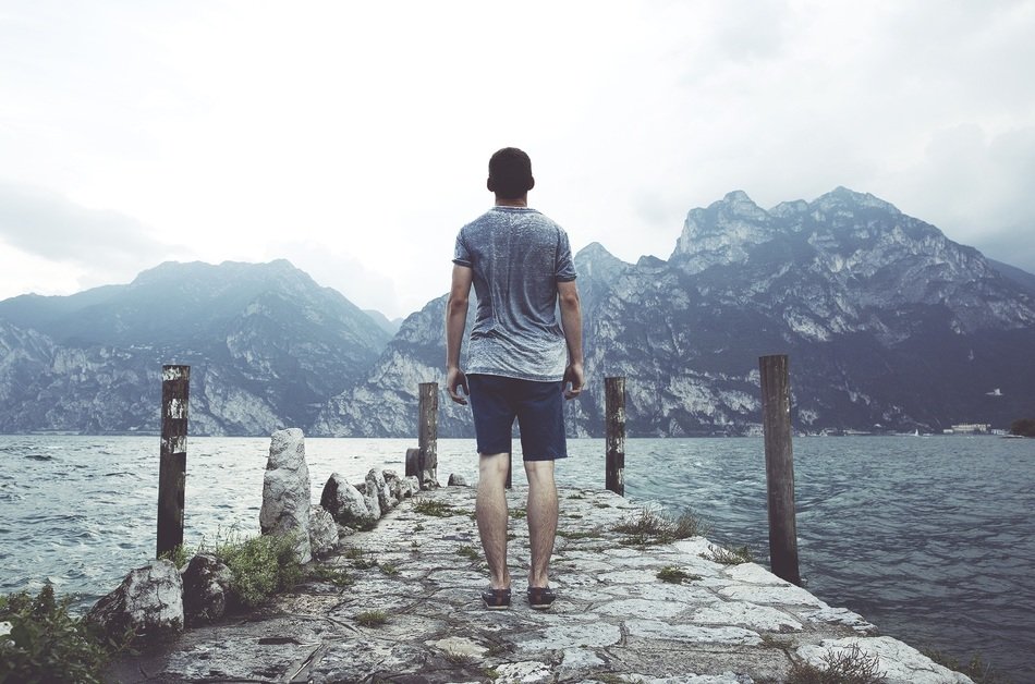 Young man by lake near the beautiful mountains under cloudy sky