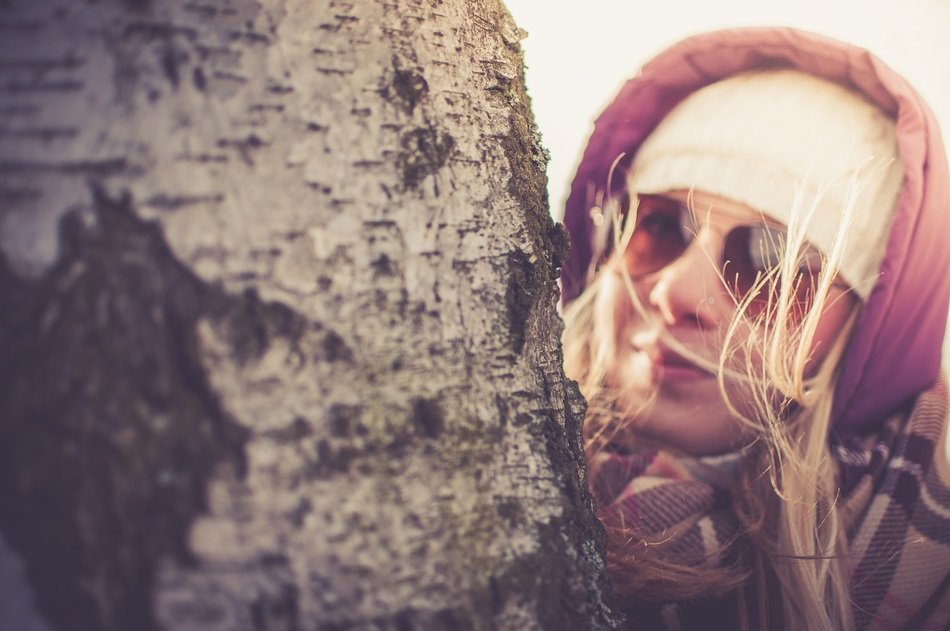portrait of girl in the hood looks out from behind a tree
