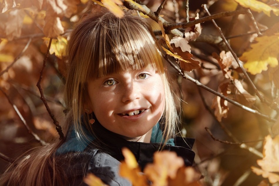 smiling blonde girl face in autumn tree leaves