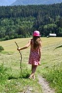 girl in pink hat with stick in hand country view