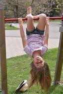 Child girl doing gymnastics head down on the crossbar