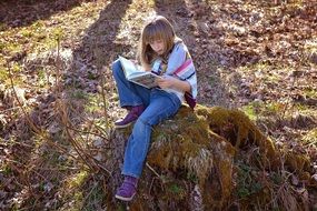 photo of Little girl is reading a book outdoors