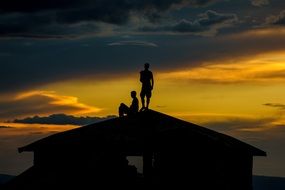 two menâs silhouettes on roof at sunset sky