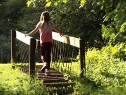 girl walks over a rickety bridge