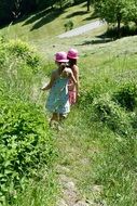 Two children walking on a trail among green grass