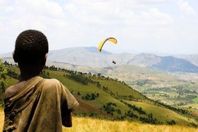 African boy stands on the mountain and looks at the parachute in the sky