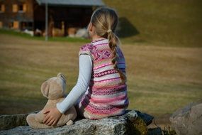 girl and teddy bear soft toy sitting on stone