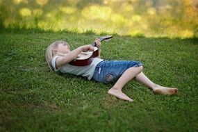 A child with a guitar lies on the grass