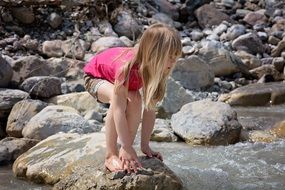Little girl with long hair among the stones near the pond