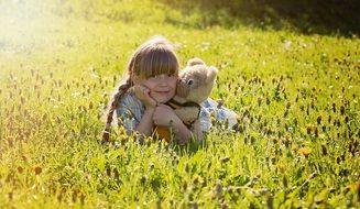 Little girl with a teddy bear among the meadow on a sunny day